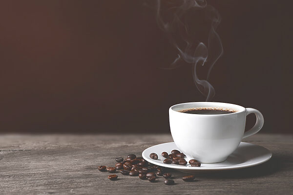 A cup of coffee with smoke and beans on a wooden surface