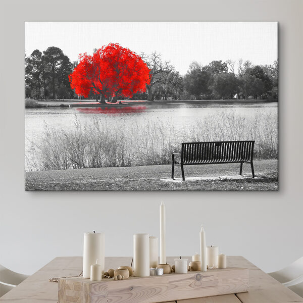 A bench by a lake with a red tree